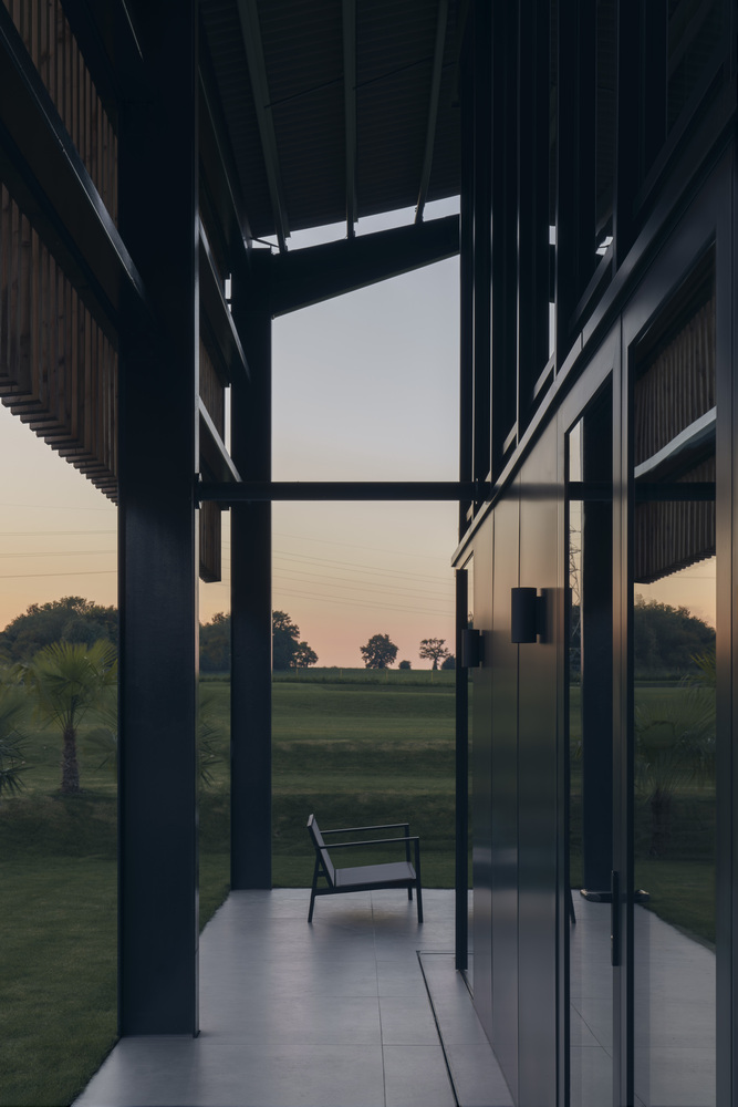 Covered terrace at dusk with exposed steel columns and clerestory window framing the darkening fields beyond