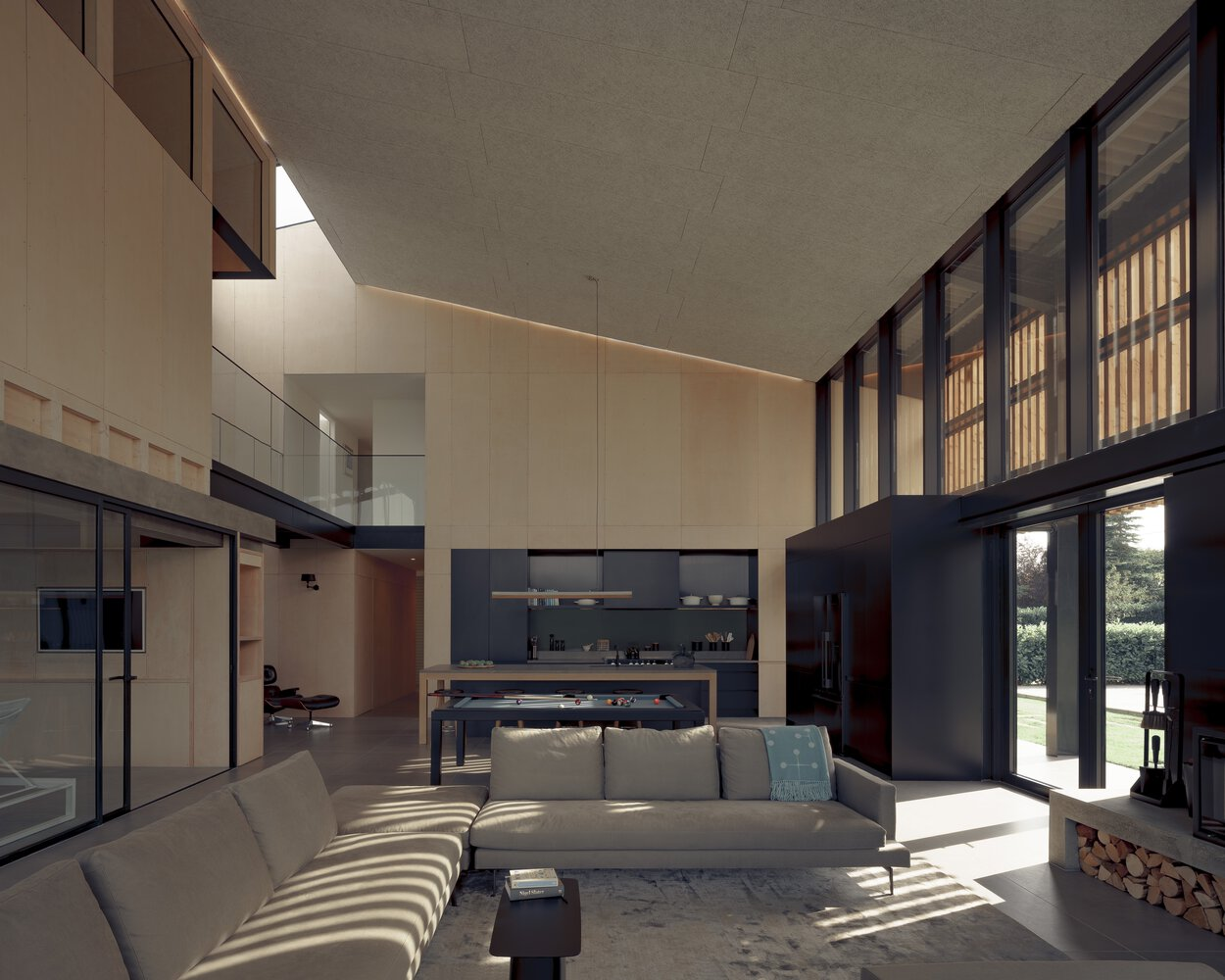 Open-plan living area with sloped concrete ceiling and continuous clerestory strip casting slatted shadows across the floor