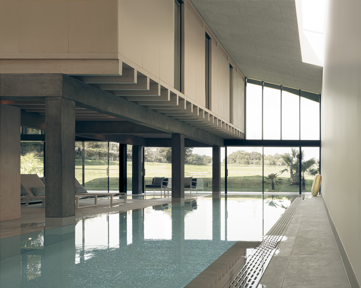 Indoor pool alongside concrete columns and exposed beam structure under a bright sky