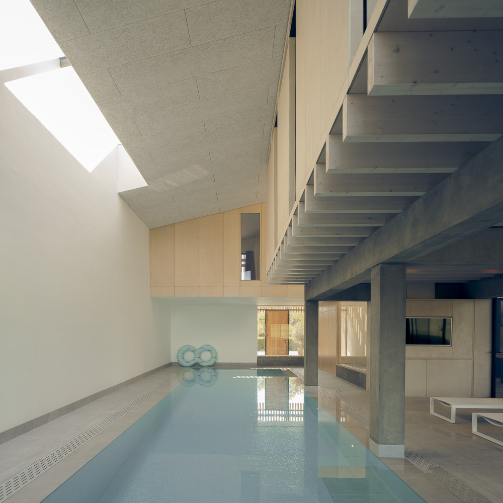 Swimming pool beneath a skylit double-height space with concrete structure above