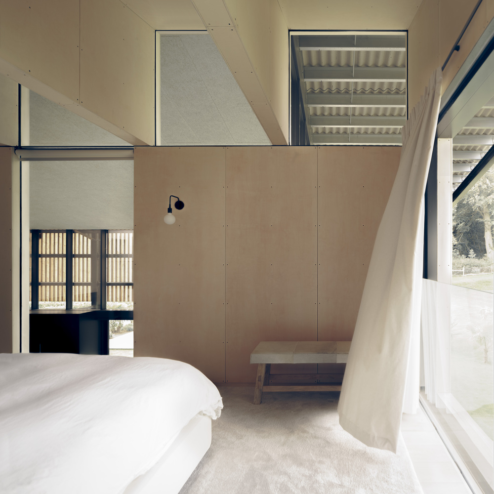 Bedroom with plywood paneling and a view through slatted screens to the landscape