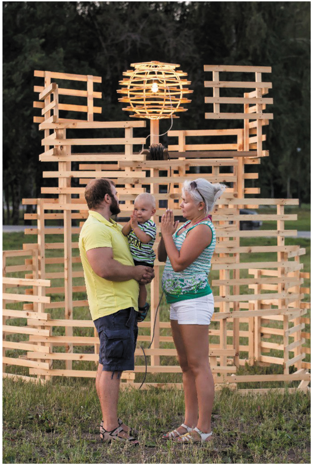 Family of three standing before the illuminated spherical lantern at the center of the timber pavilion