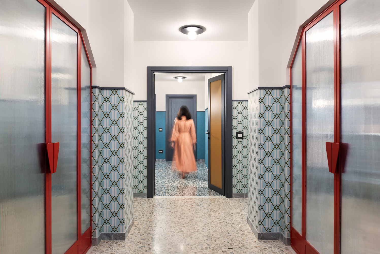 Corridor with red-framed glass doors, patterned screens, and a figure in motion through the threshold
