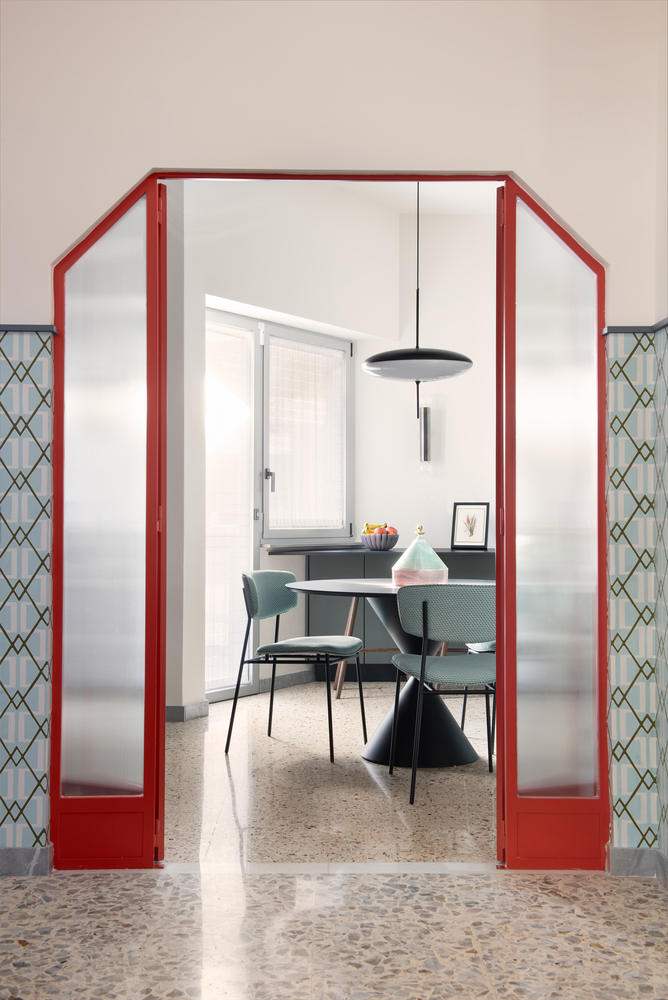 View through angled red-framed door to dining area with pendant light and terrazzo floor