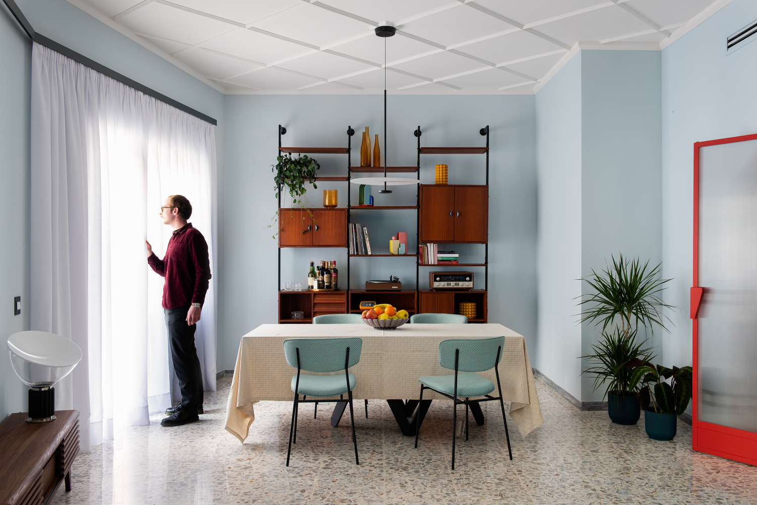 Dining room with wall-mounted shelving unit, coffered ceiling, and resident by the window curtain