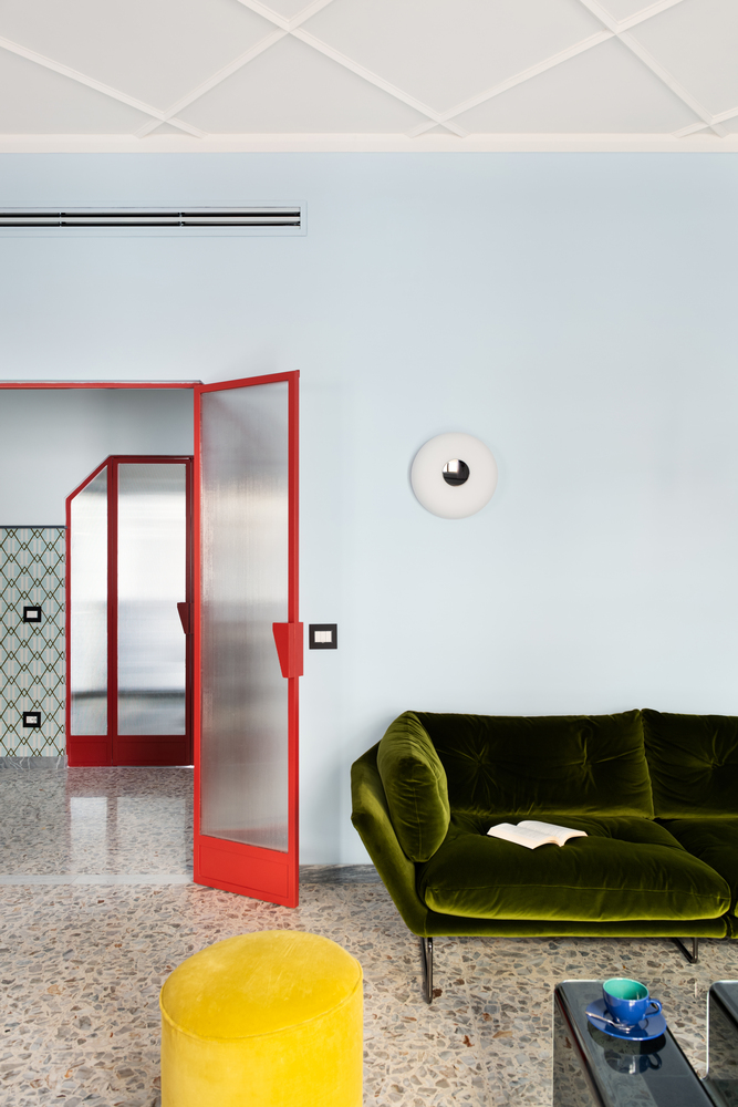 Open red-framed glass door beside pale blue wall with circular wall sconce above terrazzo floor