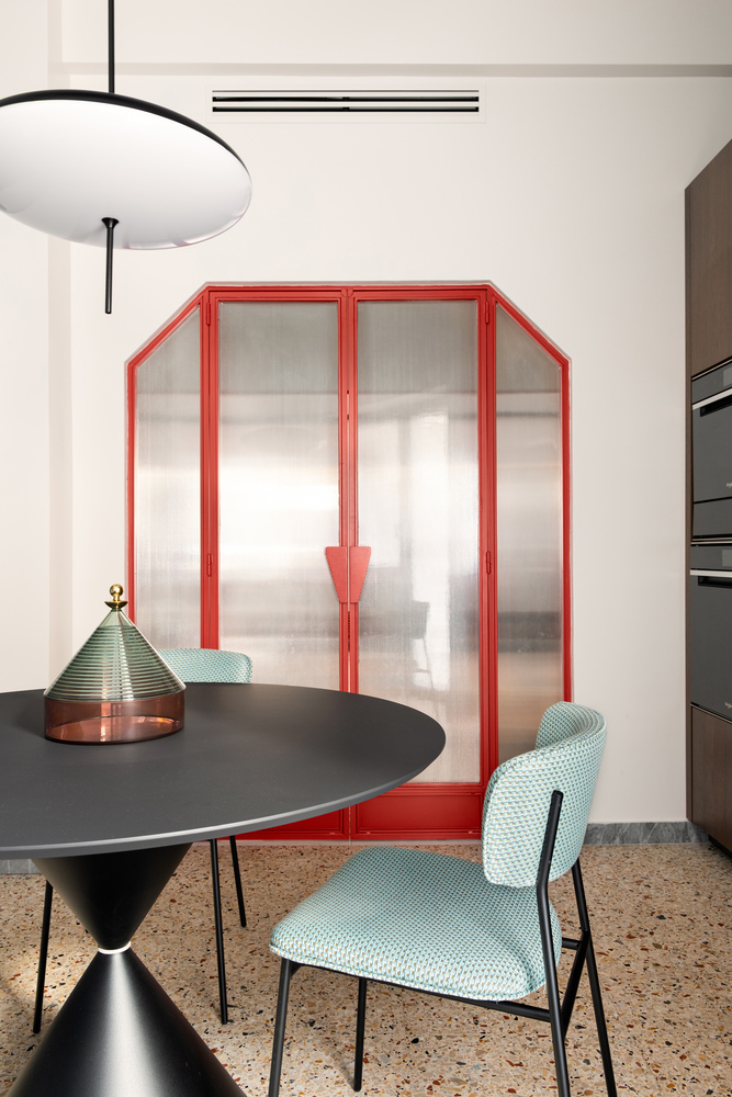 Red-framed translucent glass partition separating the kitchen from the dining area with round pendant above
