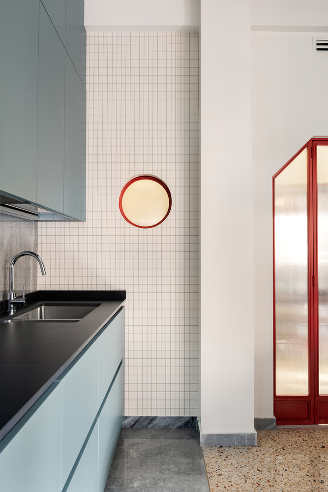 Kitchen detail with white mosaic tile wall, circular red-framed mirror and translucent red-framed partition