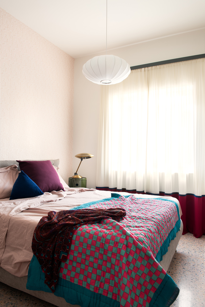 Bedroom with white paper pendant lamp, sheer curtains and layered textiles on the bed