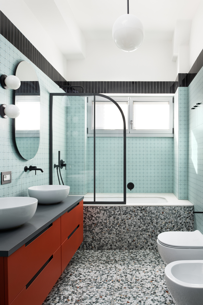Bathroom interior with mint green tile walls, terrazzo floor, orange vanity, and arched shower enclosure