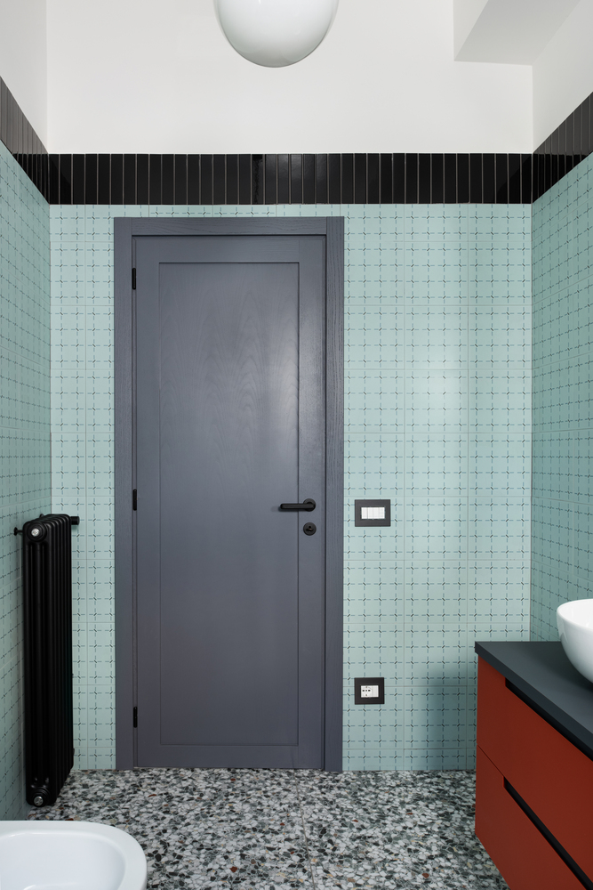 Grey door flanked by mint tile walls above terrazzo flooring with a black radiator