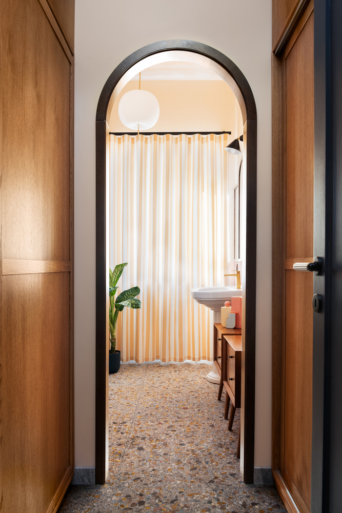 Arched doorway framed by timber cabinetry looking into bathroom with striped curtain and potted plant
