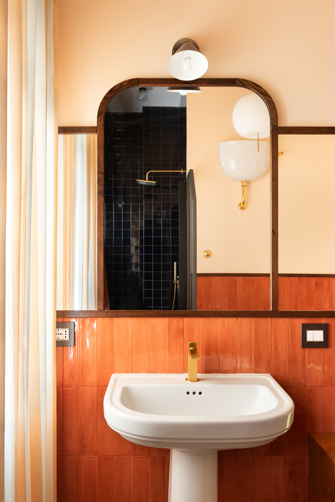 Bathroom with orange tile wainscoting, arched mirror, pedestal sink and black tiled shower niche