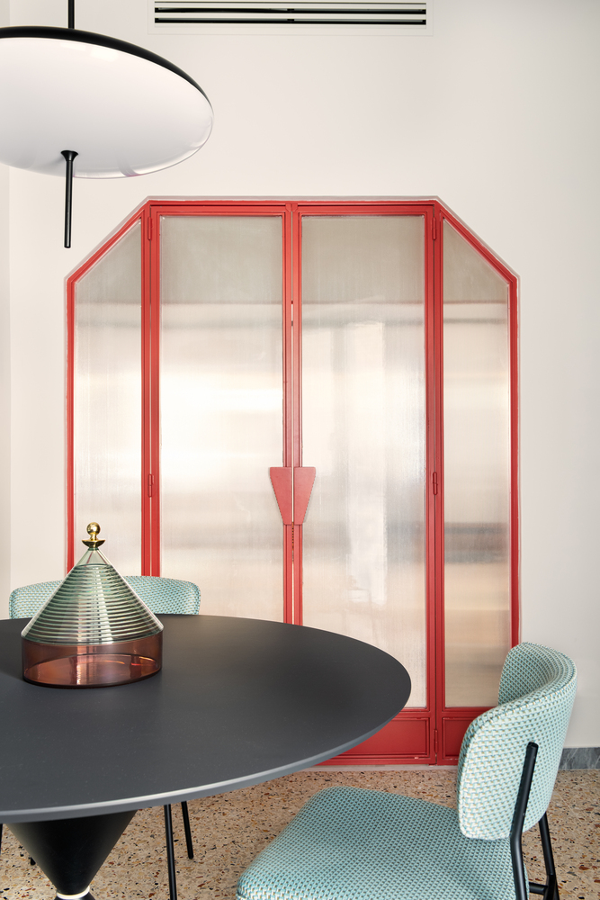 Red-framed translucent door with chevron handle beside a black dining table