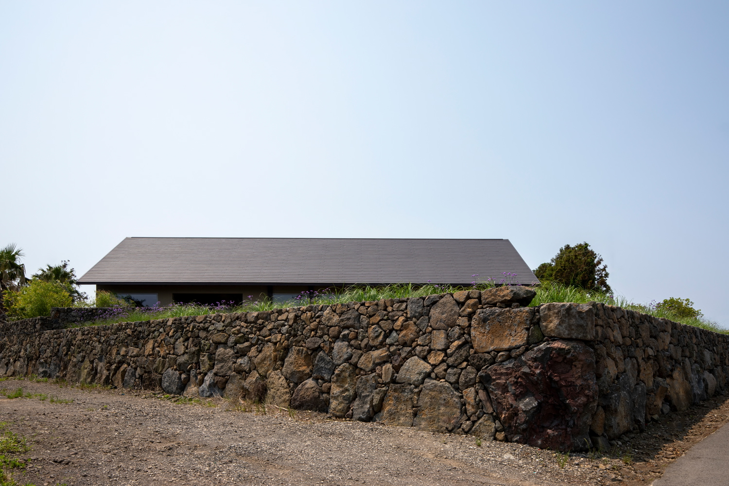 Low-profile pitched roof structure atop terraced volcanic stone retaining walls with gravel path