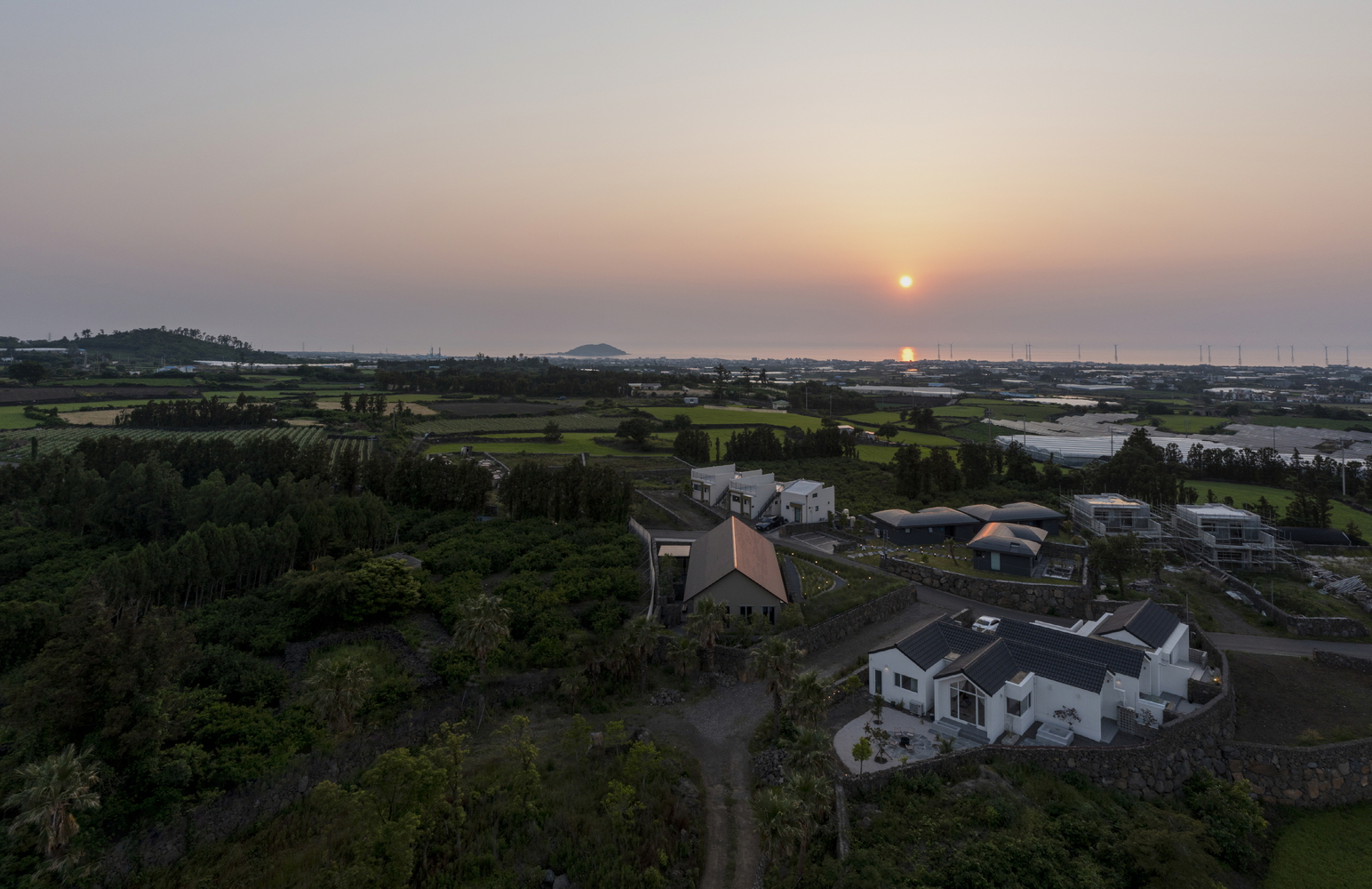Aerial view of gabled rooflines among rural fields and coastline at sunset