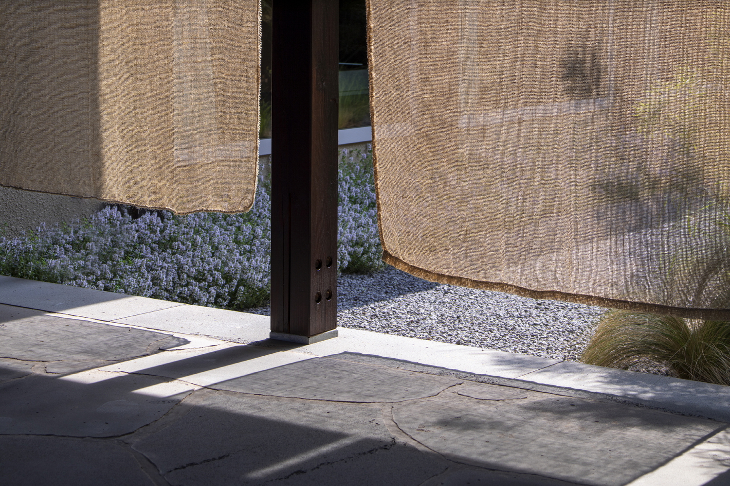 Steel column base meeting stone pavers and gravel planted bed beneath textured rammed earth walls