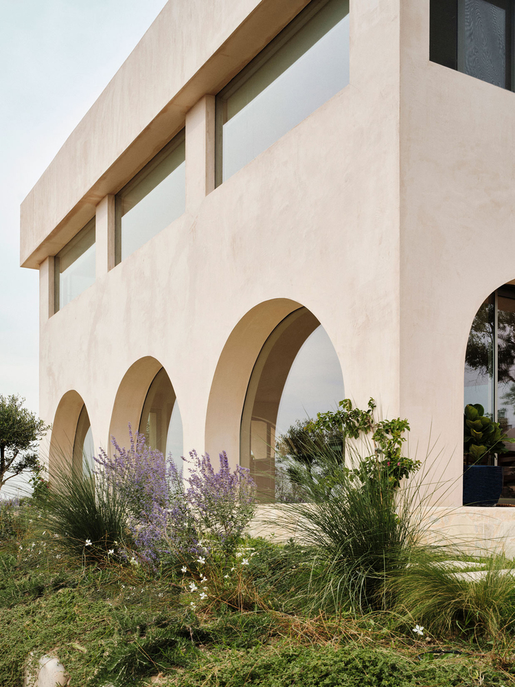Exterior view of stuccoed facade with three arched openings and planted beds of lavender and grasses