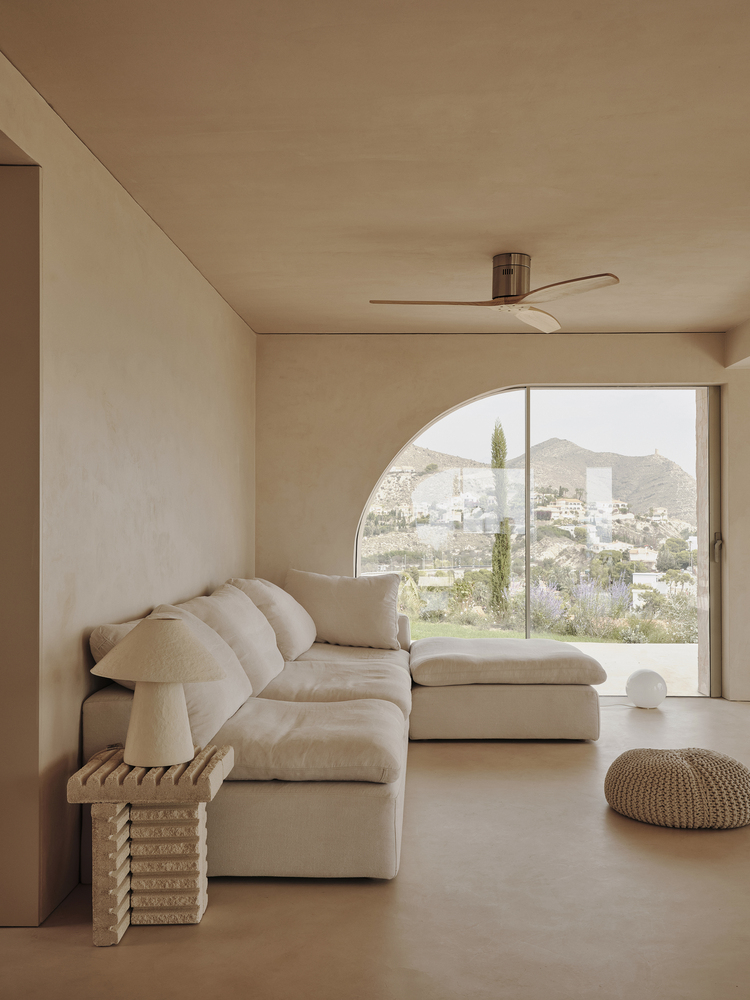 Living room with arched window overlooking hillside landscape and modular seating beneath ceiling fan