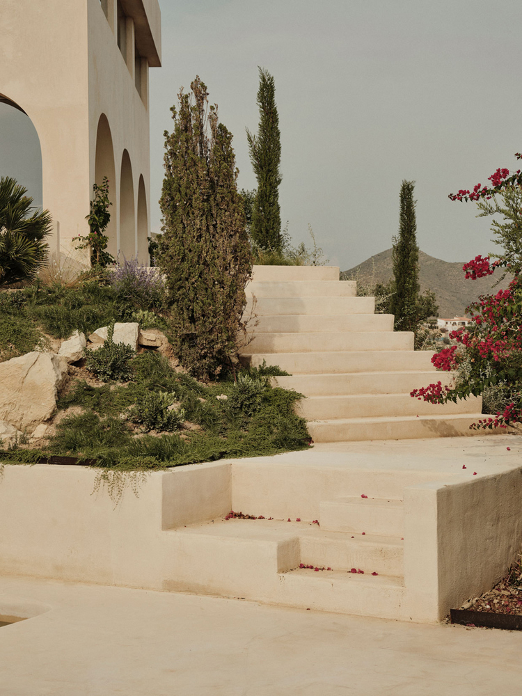 Stone staircase threading through planted beds of cypress and bougainvillea with distant mountain views