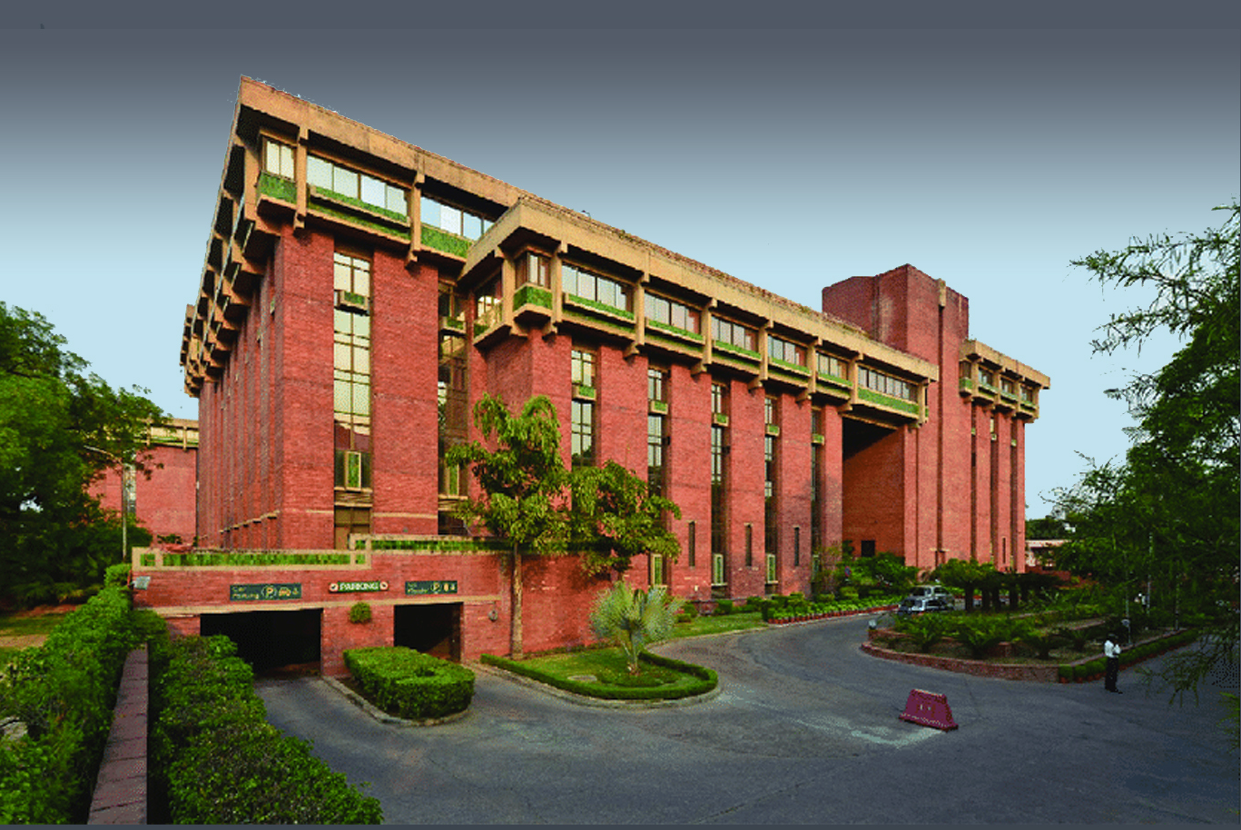 Red brick facade with exposed timber beams and planted terraces flanked by mature trees at dusk