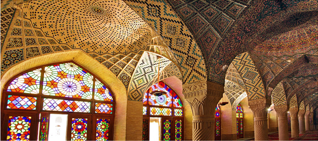 Vaulted prayer hall with brick columns, perforated ceiling and colored glass windows filtering daylight