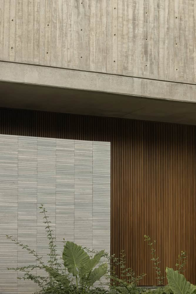 Board-formed concrete canopy above a travertine tile wall and vertical timber screen with tropical plantings