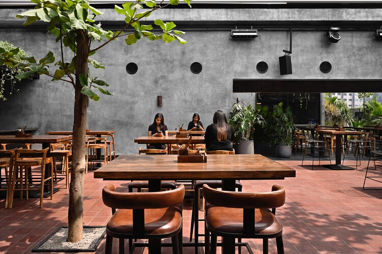Open-air dining courtyard with concrete wall punctured by circular openings and a planted tree