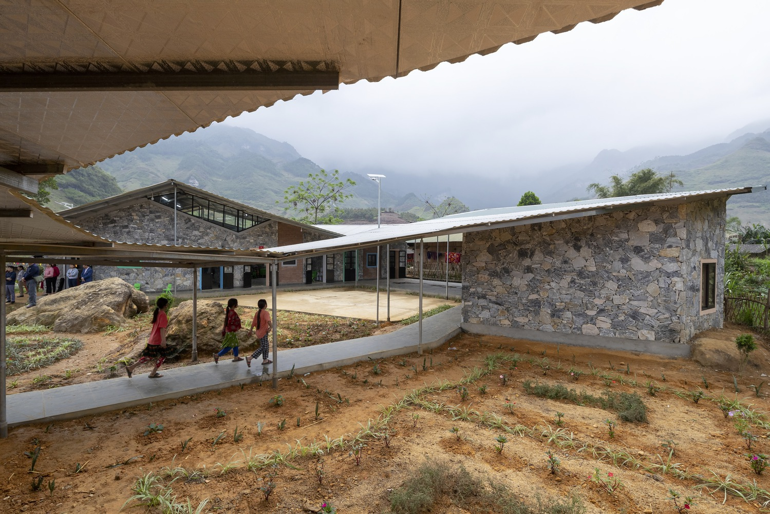 View across courtyard showing stone volumes with overhanging eaves and planted beds with misty mountains beyond