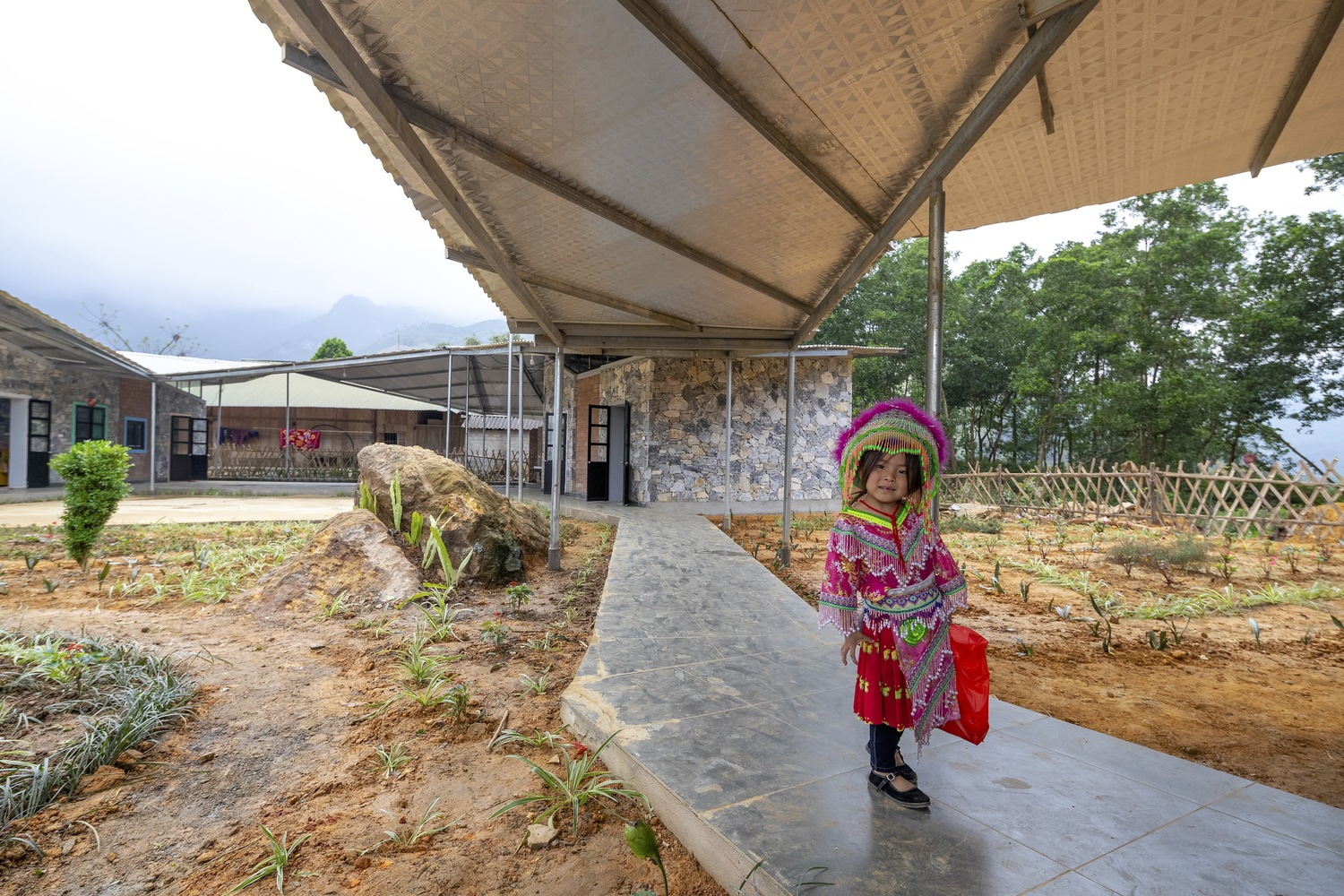 Concrete walkway beneath a corrugated roof canopy with a child walking alongside a planted bed