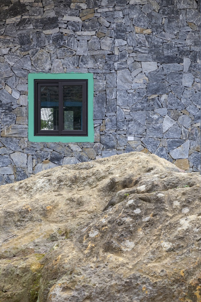 Green-framed window set into irregular grey stone wall above a weathered boulder outcrop