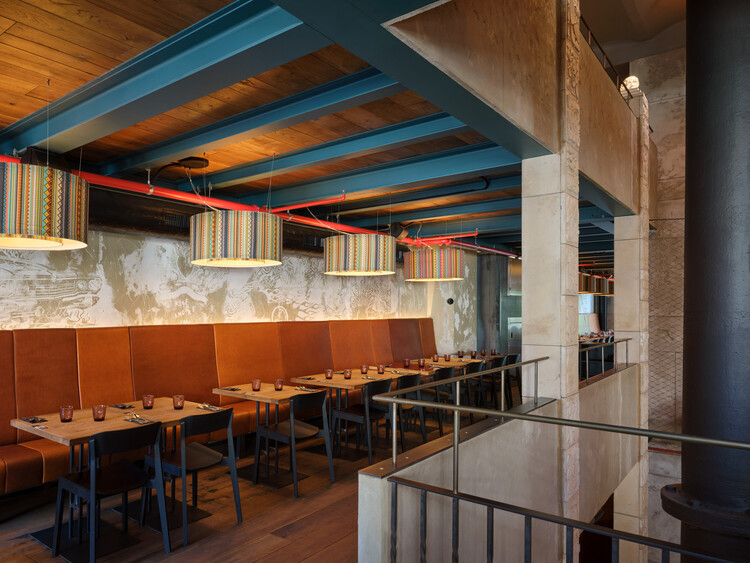 Banquette seating row along a concrete wall beneath timber joists with red conduit piping