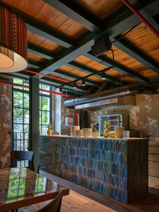 Reception desk with blue ceramic tile front beneath exposed timber ceiling and ductwork