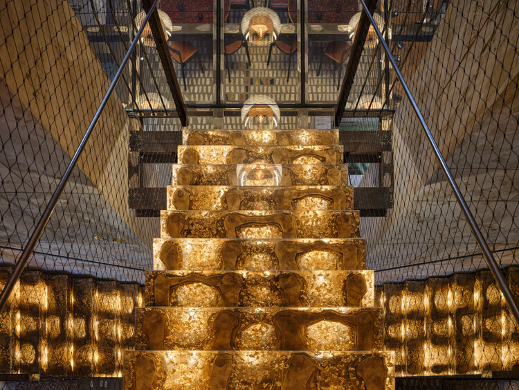 Looking up at an illuminated stepped tower of onyx panels surrounded by metal mesh railings