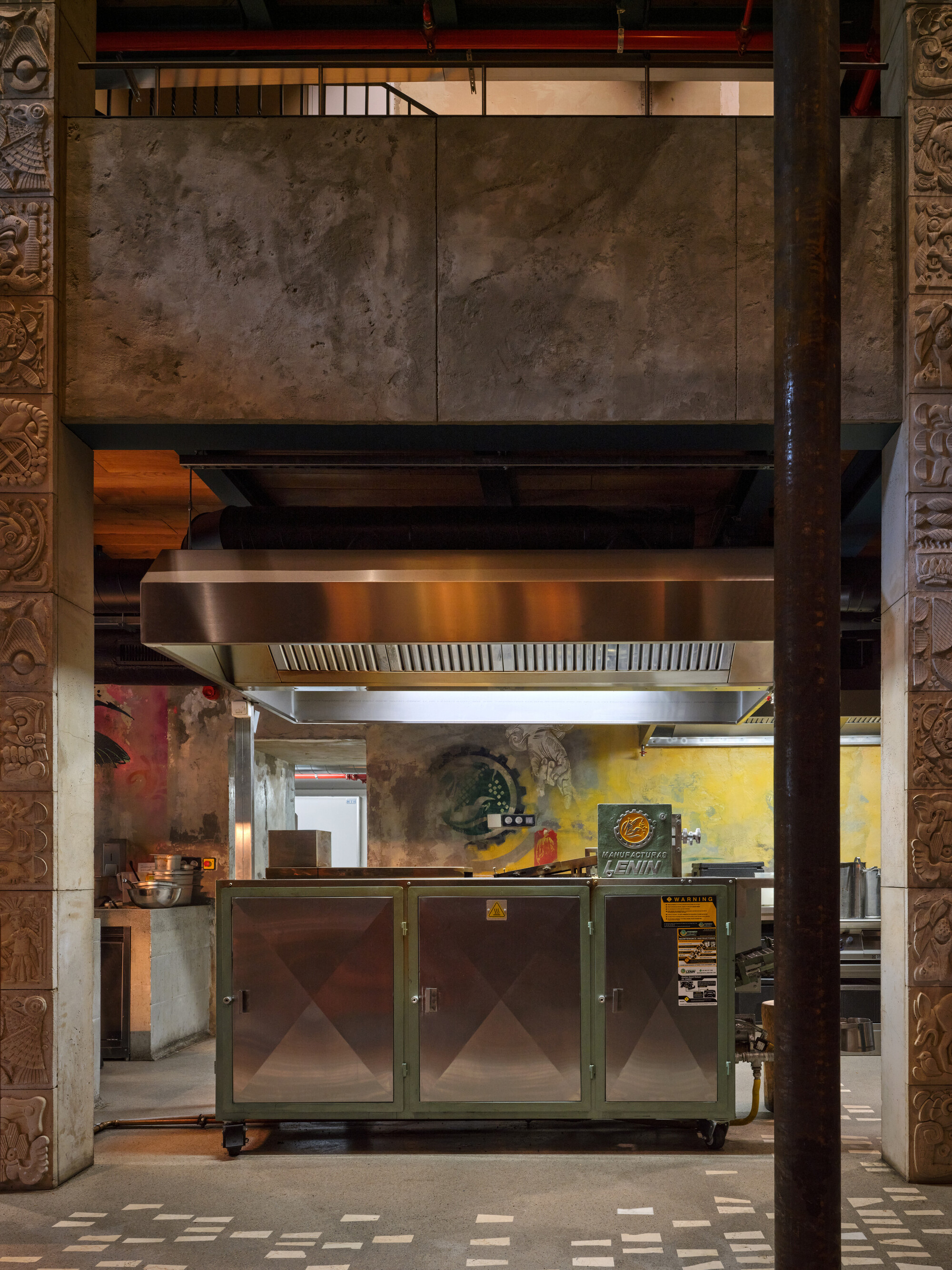 Open kitchen with stainless steel hood and equipment framed by travertine panels and carved columns
