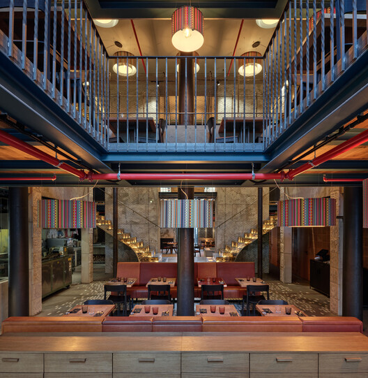Double-height dining hall with central column, mezzanine railings, and exposed red conduit pipes