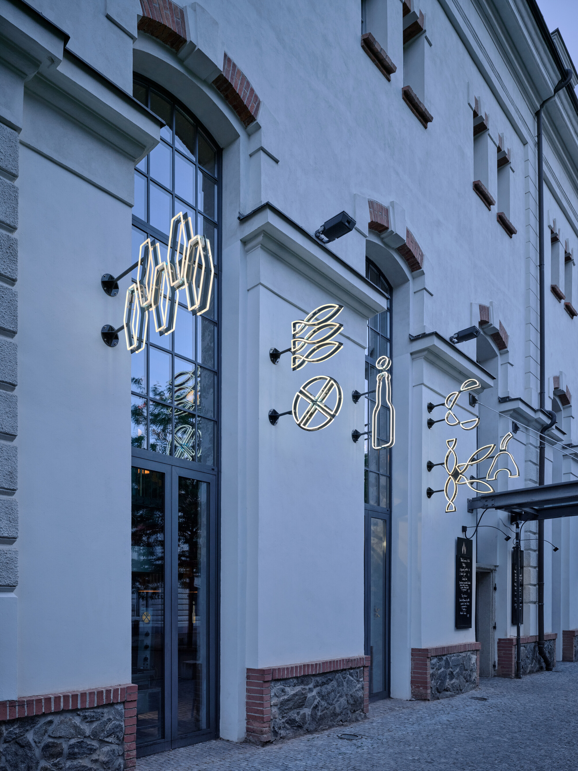 Street facade with neon food symbols mounted on white plaster at dusk