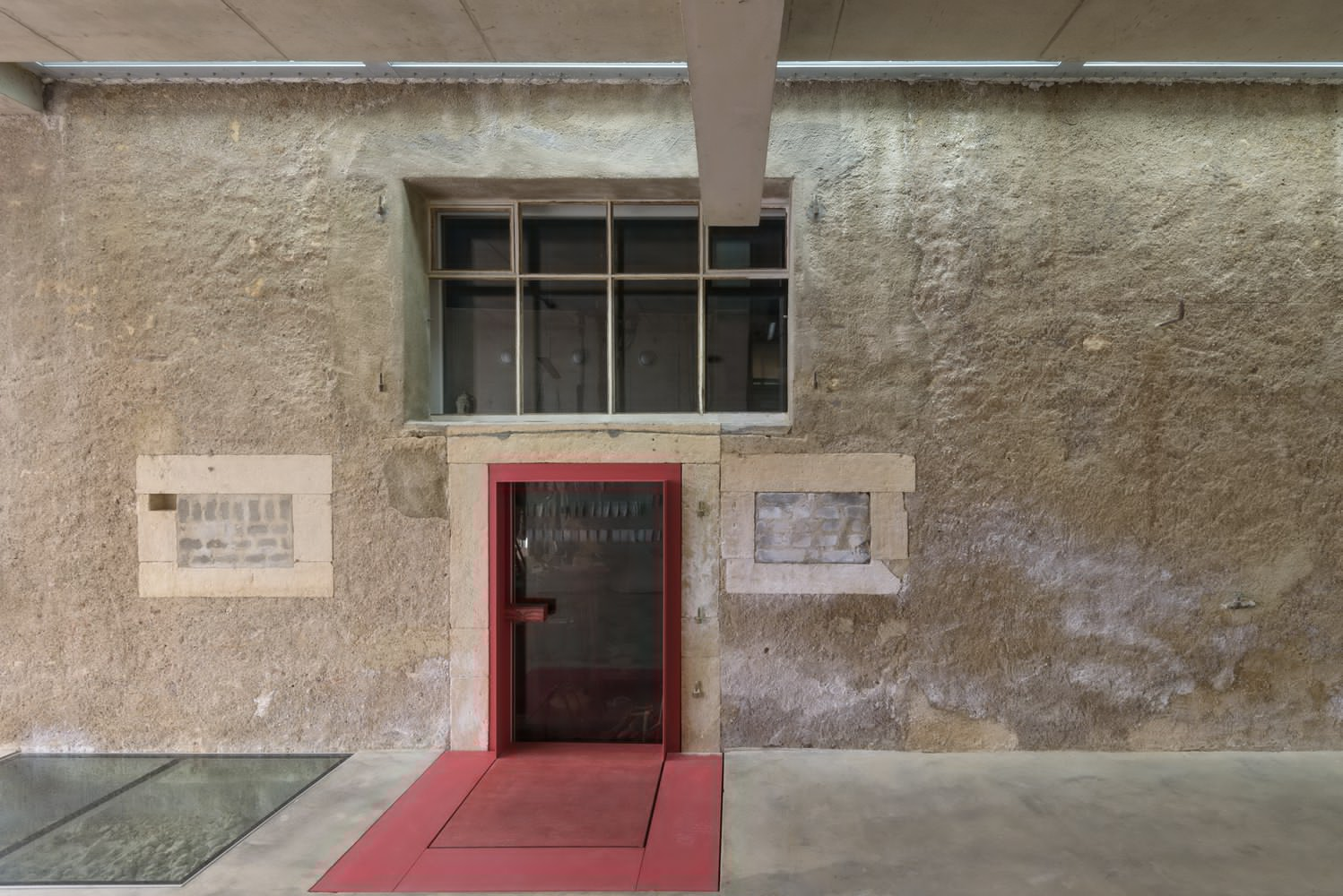 Red steel entry threshold and door set into weathered stone facade with commemorative plaques