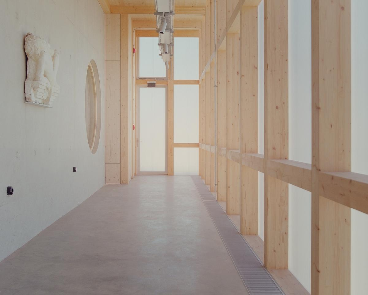 Interior corridor with exposed timber framing and translucent panel partitions on polished concrete floor
