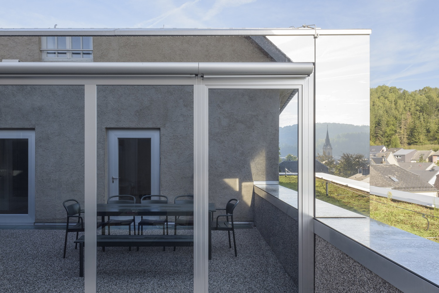 Rooftop terrace with glass balustrade and dining furniture overlooking a church spire and village