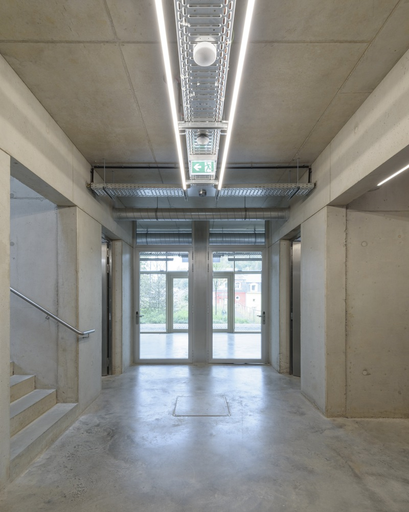 Concrete entrance foyer with exposed ceiling ducts and linear skylights framing glazed doors to the courtyard