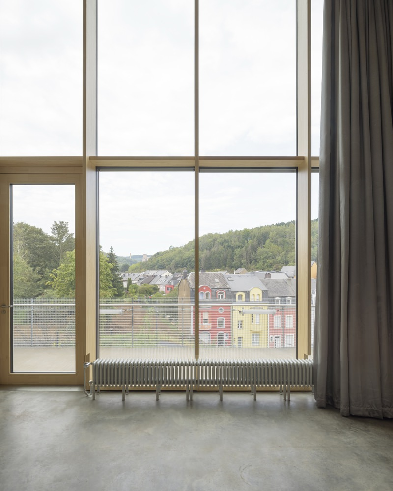 Floor-to-ceiling window with timber frame overlooking residential rooftops and forested hillside