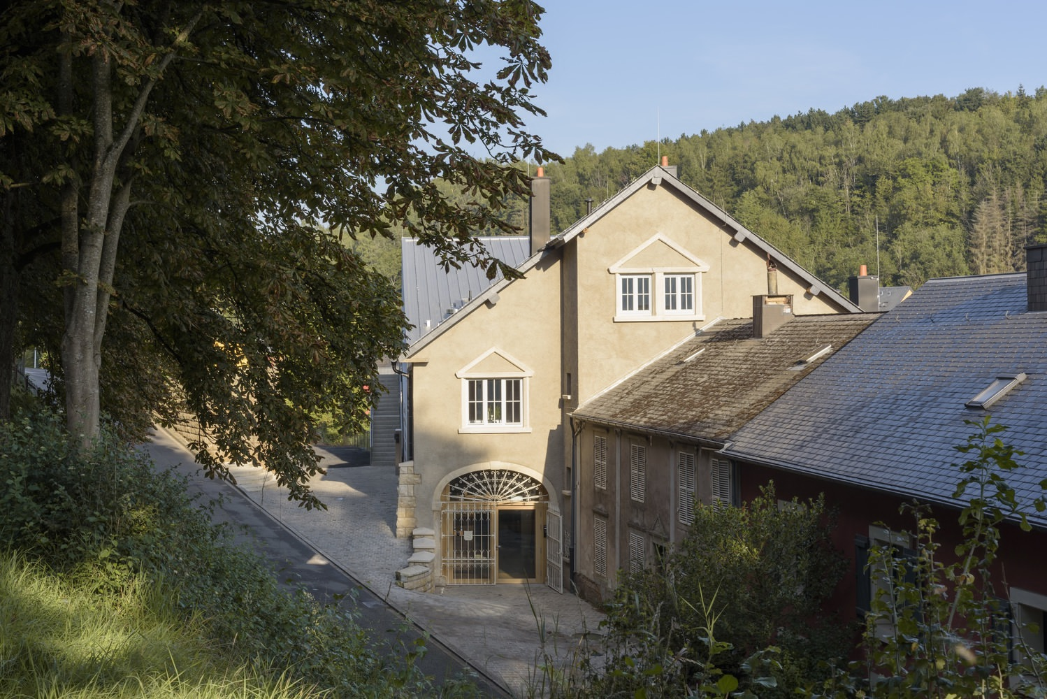 Courtyard view showing traditional gabled facade alongside timber outbuilding with forest backdrop