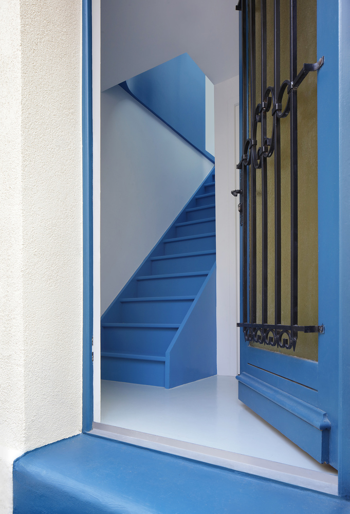 Blue painted timber door opening onto white vestibule with blue stair and green-striped exterior shutters