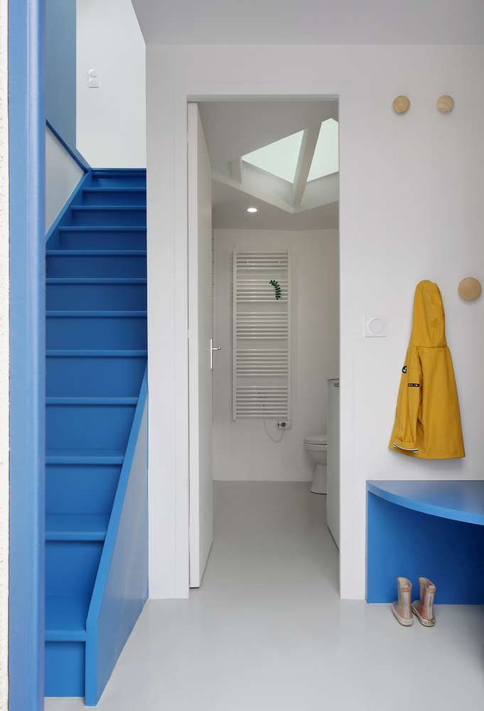 White corridor connecting blue stair and bathroom with skylight beyond yellow raincoat and wall hooks