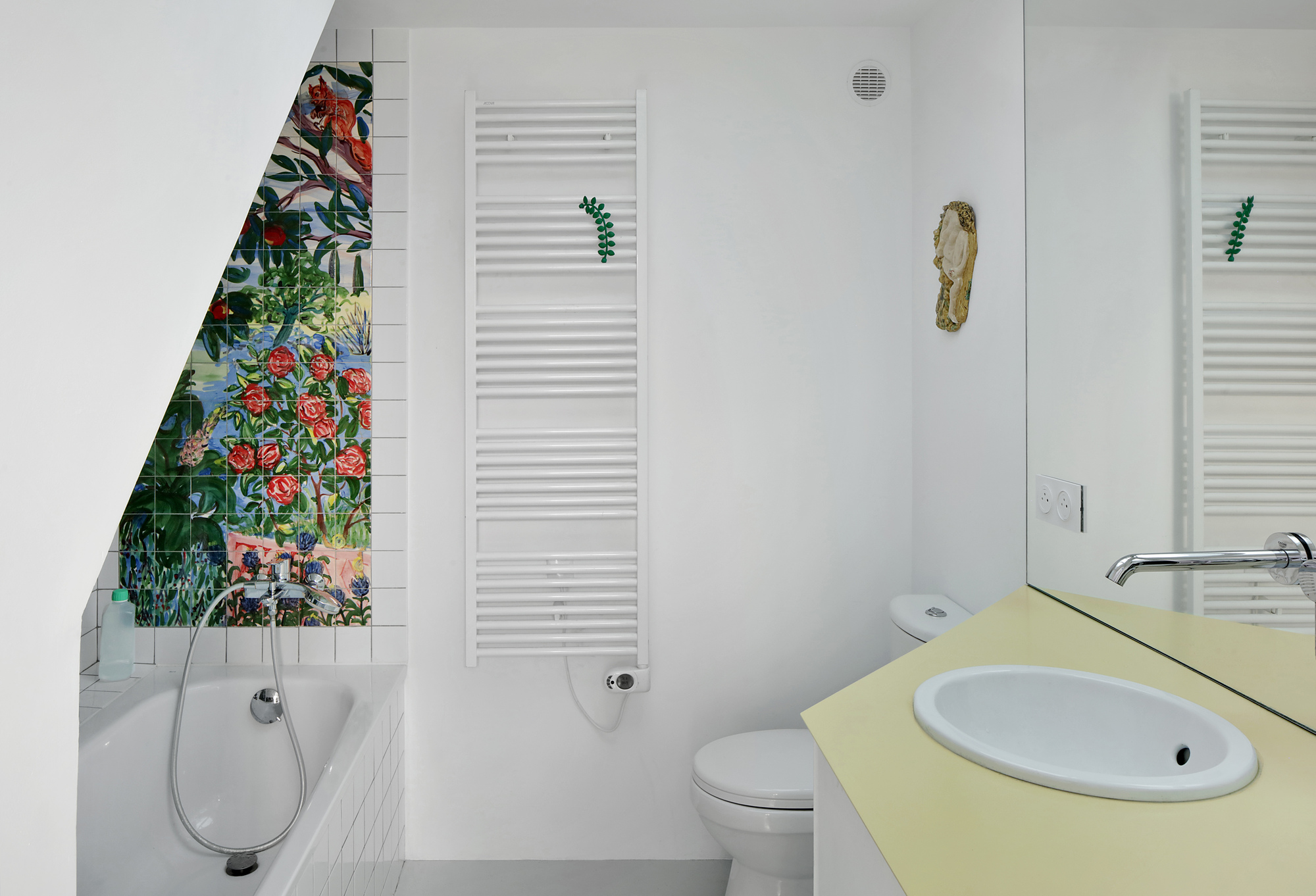 White bathroom with floral mosaic tile niche beside the tub and pale yellow vanity counter