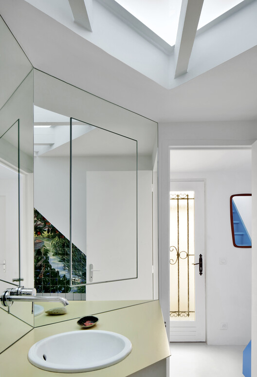 Bathroom with angled mirror above pale yellow sink counter and exposed ceiling beams in daylight