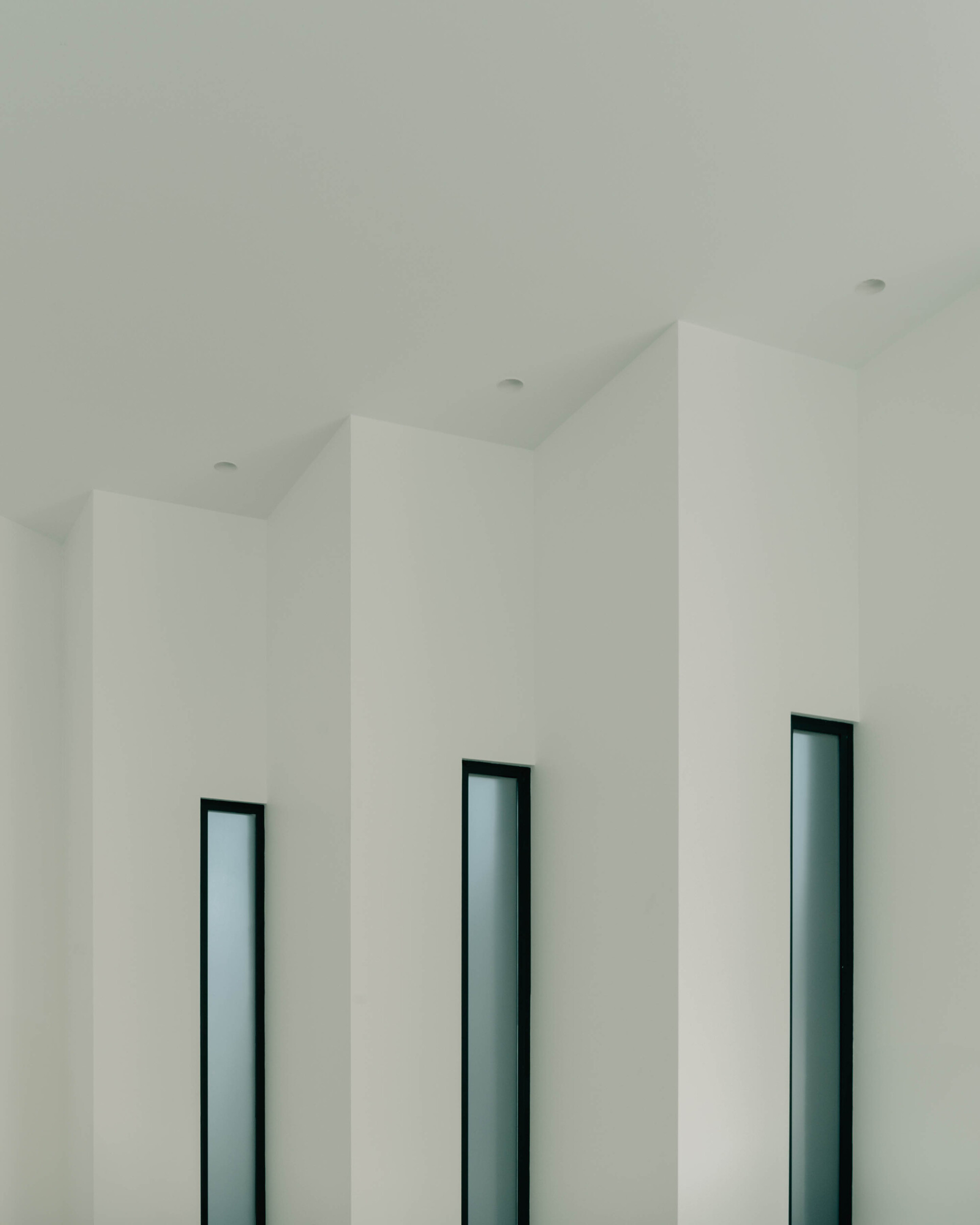 Three vertical window openings with dark frames set into white folded ceiling planes