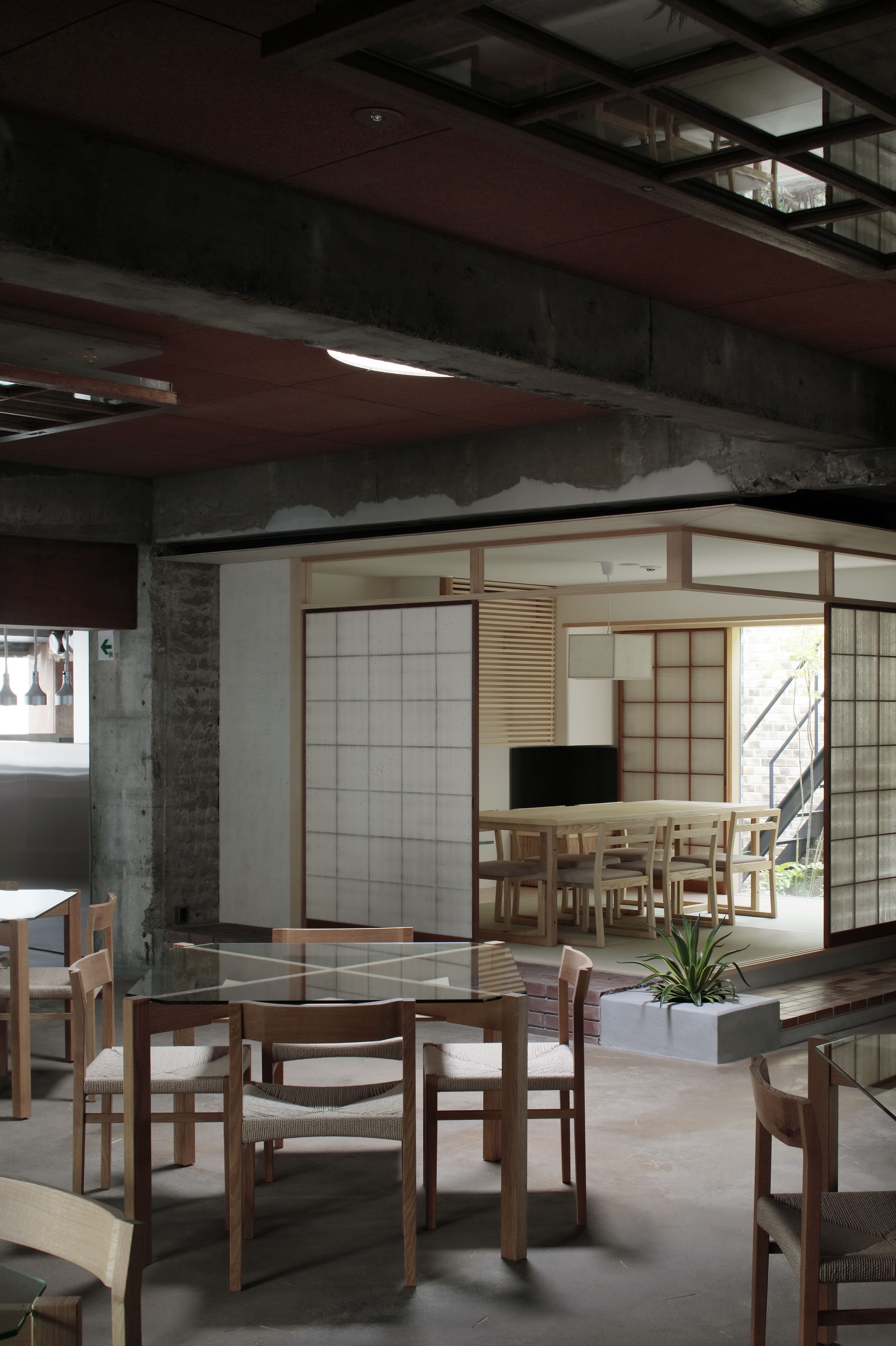 Dining area with timber chairs and tables beneath gridded ceiling fixture and exposed concrete beams