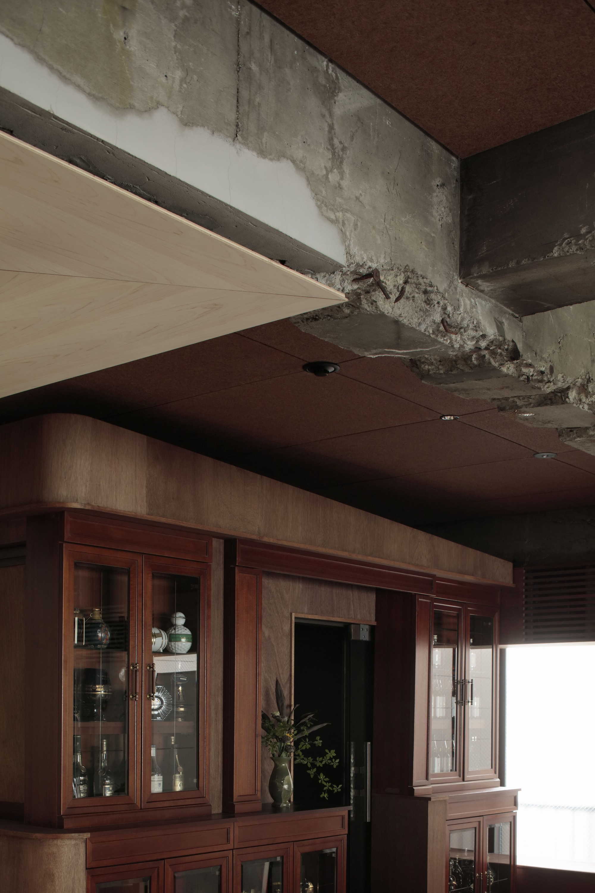 Detail of raw concrete beam meeting wood ceiling panels above dark timber display cabinets